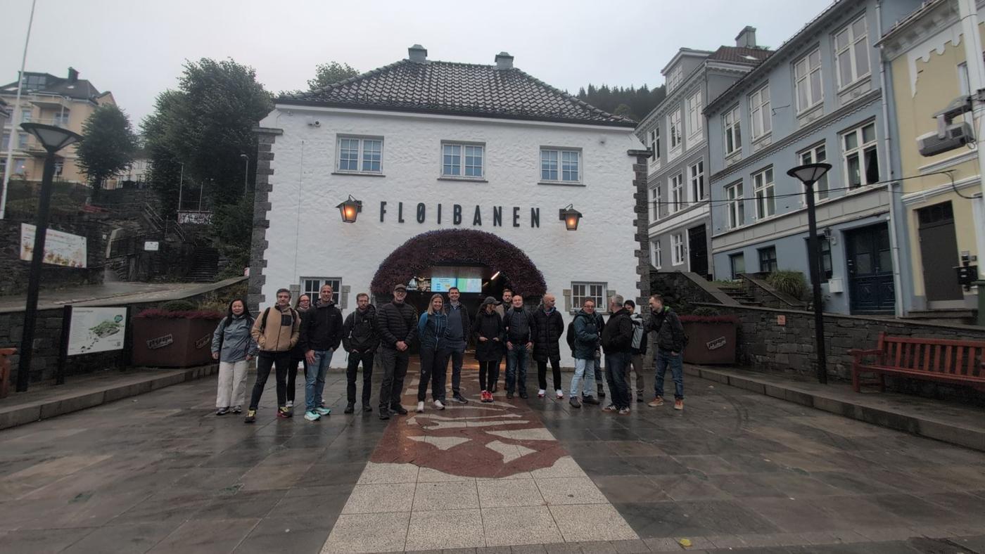A group of around twenty people in rain jackets standing in front of the arched entrance of the Fløibanen station.